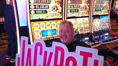 Man holding jackpot sign in front of $13,000 jackpot. 