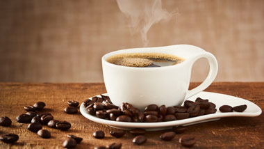 cup of steaming coffee on a wooden countertop surrounded by coffee beans