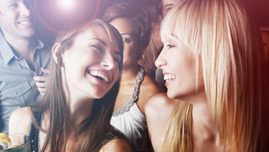 two ladies dancing with drinks in a crowd